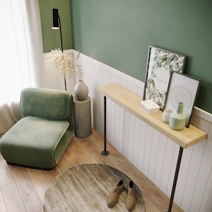 Può includere: Scena d'interni moderna con una poltrona verde, una consolle in legno con gambe in metallo nero e opere d'arte incorniciate. Un tappeto rotondo, una lampada da terra e vasi decorativi completano l'arredamento elegante e minimalista. La tavolozza dei colori comprende tonalità verdi, beige e marroni.