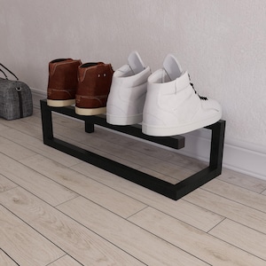 Könnte beinhalten: Ein schwarzes Schuhregal aus Metall mit zwei Schuhpaaren. Zwei braune Lederstiefel und zwei weiße High-Top-Sneaker sind auf dem Regal platziert. Das Regal ist rechteckig und steht auf einem hellen Holzboden.