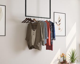 May include: A black metal clothing rack suspended from the ceiling, holding various garments on wooden hangers. The clothes include a white top, a tan cardigan, a checkered shirt, a red sweater, and a denim shirt. Artwork and plants are in the background.
