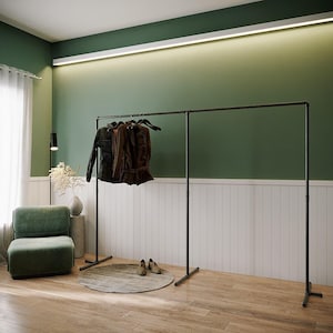 Puede incluir: Un perchero de metal negro con varias chaquetas colgadas en perchas de madera. Las chaquetas son de varios tonos de marrón y negro. Un sillón verde y una alfombra redonda están en primer plano. La pared es verde y blanca.