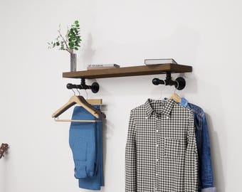 Wall-mounted industrial shelf with a wooden shelf and metal pipe fittings, featuring a hanging rail for clothes storage.
