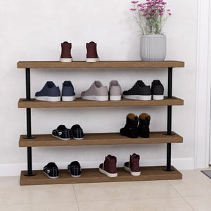 Könnte beinhalten: Ein vierstöckiges Schuhregal mit dunklen Holzregalen und schwarzen Metallstützen. Auf den Regalen sind verschiedene Schuhe, darunter Turnschuhe und Stiefel, ausgestellt. Auf dem obersten Regal steht eine Topfpflanze mit lila Blüten.