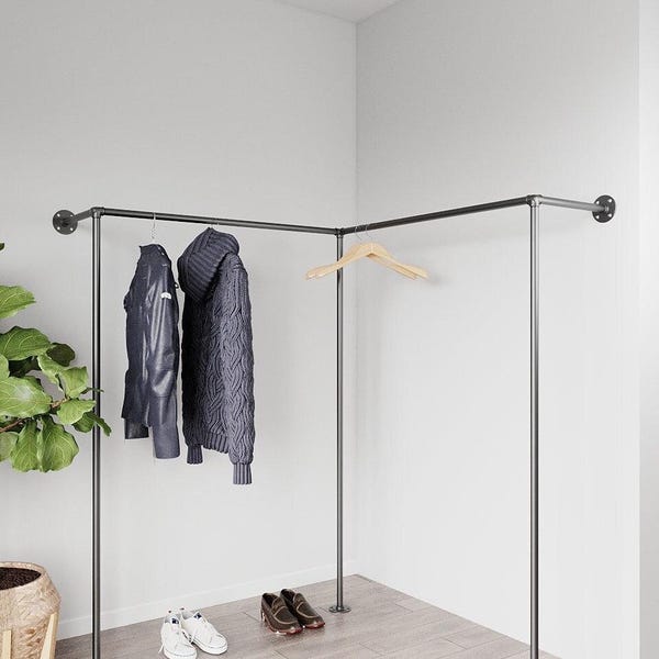 Könnte beinhalten: Ein dunkler Metall-Kleiderständer mit Eckdesign. Eine schwarze Lederjacke und ein grauer Strickpullover hängen an dem Ständer. Weiße Turnschuhe und braune Schuhe stehen auf dem Boden. Ein Holzkleiderbügel ist ebenfalls vorhanden.