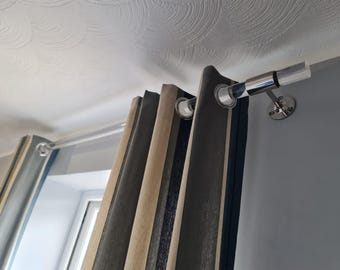 May include: Curtains with a striped pattern in shades of gray, beige, and black are hung from a silver curtain rod. The rod is mounted on the ceiling with silver brackets. The curtains are partially open, revealing a window.