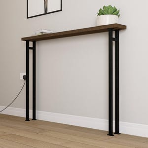 Pode incluir: Uma mesa de consola moderna com um tampo de madeira castanha escura e pernas de metal preto. A mesa tem aproximadamente 152 cm de comprimento e apresenta um design minimalista. Uma pequena planta em vaso e livros estão na mesa.