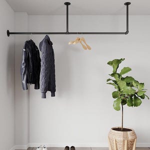 May include: Black metal clothes rail suspended from the ceiling, with a black leather jacket and a grey sweater hanging. A potted plant and two pairs of shoes are on the floor.