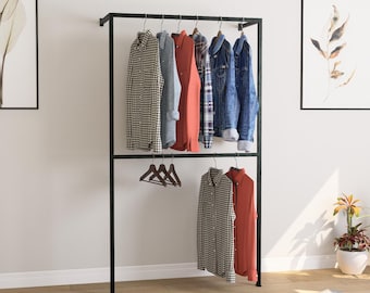 May include: A black metal clothing rack with two levels, holding various shirts and jackets. The garments include a checkered shirt, denim jacket, and solid-colored shirts in red and blue. Wooden hangers are used.