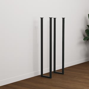 Puede incluir: Cuatro patas de mesa de metal negro con un diseño moderno y minimalista. Las patas son rectangulares y tienen una base en forma de U. Son adecuadas para varios tamaños y estilos de mesa, ofreciendo una estética elegante e industrial. Las patas se muestran contra una pared blanca y un suelo de madera.