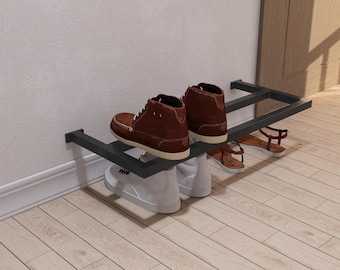 Könnte beinhalten: Ein dunkelgrauer Schuhständer aus Metall an einer weißen Wand, der verschiedene Schuhe hält. Zwei braune Lederstiefel, weiße Turnschuhe und braune Sandalen sind zu sehen. Der Ständer hat ein minimalistisches Design.