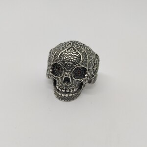 May include: A silver skull ring with intricate filigree details and red gemstone eyes.