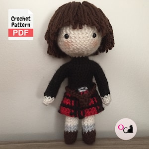May include: Crochet pattern PDF for a brown haired doll wearing a black sweater and a red and black tartan kilt. The doll has a white face with black eyes and a pink blush.