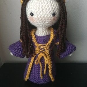 May include: Crocheted doll with long brown hair, a purple dress with yellow trim, and a gold crown.