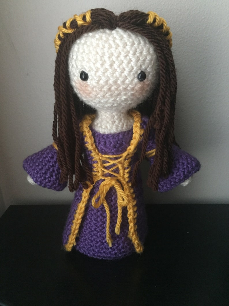 May include: Crocheted doll with long brown hair, a purple dress with yellow trim, and a gold crown.