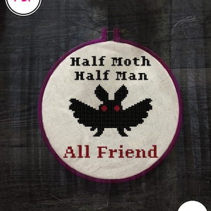 Puede incluir: Un aro de bordado blanco con un diseño bordado en negro y rojo de una polilla con el texto "Half Moth Half Man All Friend".