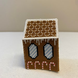 May include: A brown gingerbread house with white icing and candy cane details. The roof is decorated with gold and white beads.