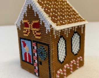 May include: A miniature gingerbread house cross-stitch with a white roof, brown walls, red and white candy canes, and a green beaded wreath on the door.
