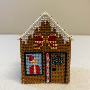 May include: A brown gingerbread house cross-stitch with a white roof, red and white candy canes, a green wreath, and a Santa Claus figure in the window.