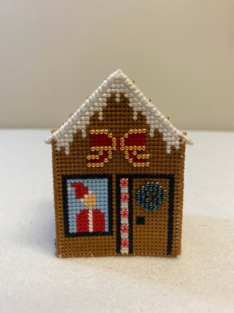 May include: A brown gingerbread house cross-stitch with a white roof, red and white candy canes, a green wreath, and a Santa Claus figure in the window.