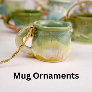 May include: A collection of small, ceramic mug ornaments with a rustic aesthetic. Each miniature mug features a handle and is adorned with a unique blend of green, yellow, and blue glazes. A twine loop is attached for hanging. The text "Mug Ornaments" is displayed.