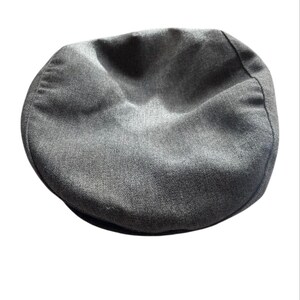 Puede incluir: Una gorra gris con una corona redondeada y una pequeña visera rígida. La gorra está hecha de una tela texturizada y es de un color liso y neutro. Este estilo clásico es adecuado para varios atuendos.