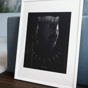 May include: A white framed print of a black and white illustration of Black Panther's mask. The print is on a black background and the text "FOREVER" is printed below the mask.