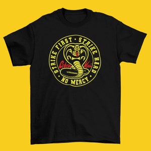 May include: Black t-shirt with a yellow circle graphic featuring a cobra with the text "Strike First Strike Hard No Mercy Cobra Kai".