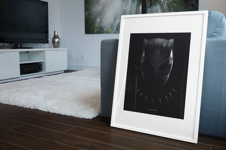 May include: A white framed print of a black and white illustration of Black Panther's mask. The print is on a black background and the text "FOREVER" is printed below the mask.