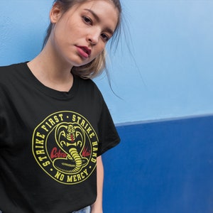 May include: Black t-shirt with a yellow circle graphic featuring a cobra with the text "Strike First Strike Hard No Mercy" and the words "Cobra Kai" in red.