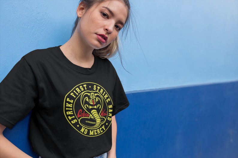 May include: Black t-shirt with a yellow circle graphic featuring a cobra with the text "Strike First Strike Hard No Mercy" and the words "Cobra Kai" in red.