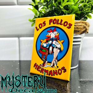 May include: A yellow rectangular magnet featuring the text "LOS POLLOS HERMANOS" in red lettering. The magnet has a blue circle in the center with two cartoon chickens wearing sombreros. The bottom of the magnet has the text "MYSTERY DECALS.COM" in a teal font.