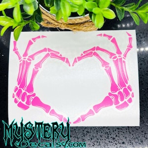 May include: Pink skeleton hands forming a heart shape. The decal is on a white background.