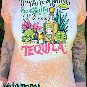 May include: Peach-colored t-shirt with a bleached design and rolled sleeves. The graphic features a tequila bottle, shot glass, lime slices, and the text "If You're Gonna Be Salty, At Least Bring Some Tequila."