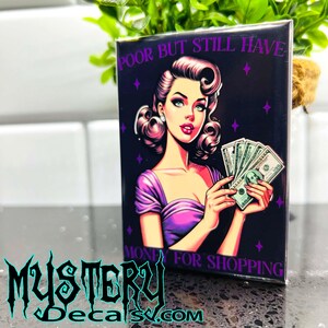 May include: A purple and black magnet with a cartoon image of a woman with a purple dress and a stack of money. The text on the magnet reads "Poor but still have money for shopping."