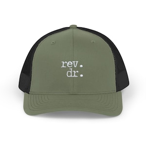 May include: Olive green trucker hat with a black mesh back. The hat features the embroidered text "rev. dr." in white. The hat has a curved brim and a snapback closure.
