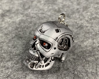 Può includere: Un portachiavi a forma di teschio di Terminator color argento con occhi rossi luminosi. Il teschio è dettagliato con parti meccaniche e ha un anello per attaccarlo a un portachiavi.