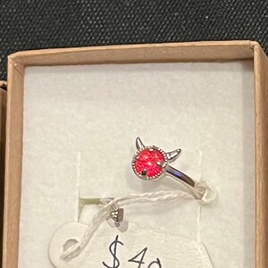 May include: A silver ring with a red stone and small horns on the top. The ring is in a small box with a price tag that says £40.