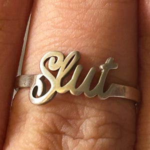 May include: A silver ring with the word "Slut" spelled out in cursive.