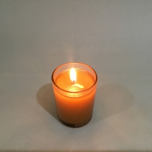 May include: A lit candle in a clear glass jar with a yellow wax. The candle is burning with a small flame.