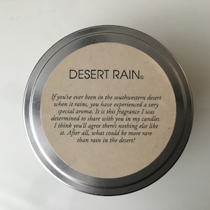 May include: A silver tin candle with a brown label that reads "DESERT RAIN." The label also includes a description of the scent, which is inspired by the smell of rain in the desert.