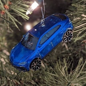 Könnte beinhalten: Ein blauer Spielzeugauto-Anhänger, der an einem Weihnachtsbaum hängt. Das Auto hat schwarze Räder und ein detailliertes Design.