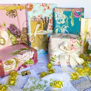 May include: A collection of wrapped gifts with floral patterns and ribbons. The gifts are arranged on a white tablecloth with yellow candies scattered around them.