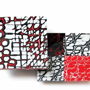 May include: Two square tiles with a black, white and red abstract pattern. The tiles are made of a smooth, glossy material.