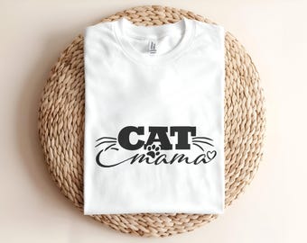 May include: A white short-sleeved t-shirt featuring the black text CAT mama printed on the front. The design includes a small paw print above the word mama, stylized whiskers extending from the word CAT, and a small heart at the end.