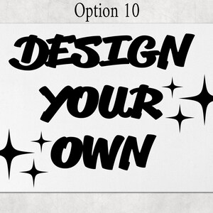 May include: A rectangular white sign featuring the black text "DESIGN YOUR OWN" in a bold, stylized font. The design is accented by several four-pointed star shapes in black, positioned to the left of the bottom word and to the right of the middle word.