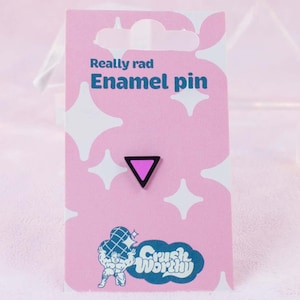 May include: A pink enamel pin with a black outline and a purple triangle design. The pin is attached to a pink card with the text "Really rad Enamel pin" and the "Crush Worthy" logo.