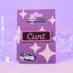 May include: A pink and black iron-on patch with the word "CUNT" embroidered in white. The patch is on a purple card with white stars and the text "Hella cute embroidered iron-on patch".