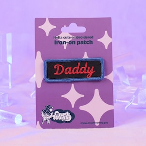 May include: A blue and black iron-on patch with red embroidered text that says "Daddy". The patch is on a purple card with white stars and the text "Hella cute embroidered iron-on patch".
