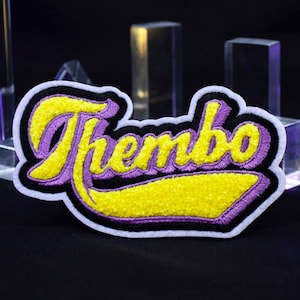 May include: A purple and yellow embroidered patch with the word "Thembo" in a cursive font.