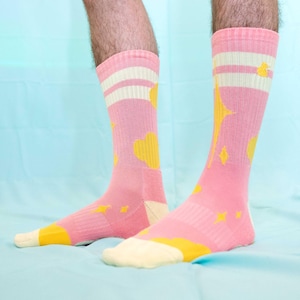 May include: A pair of pink socks with yellow abstract designs. The socks have white stripes around the ankle.