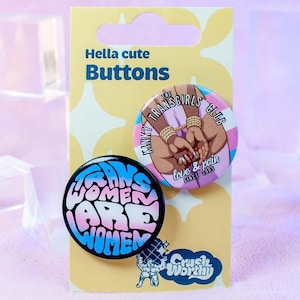 Peut inclure: Deux badges à épingle avec des slogans féministes. Le premier badge est noir avec du texte blanc et rose qui dit "Trans Women Are Women". Le deuxième badge est rose, bleu et blanc avec le texte "Trans Girls Club" et un graphique de deux femmes se tenant la main. Les badges sont sur une carte jaune avec le texte "Hella cute Buttons" et le logo "Crash Worx".